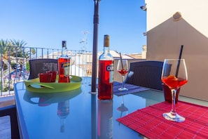 Una mesa de vidrio con una botella de Aperitivo, una copa de vino tinto y un cóctel en un balcón con vistas despejadas.