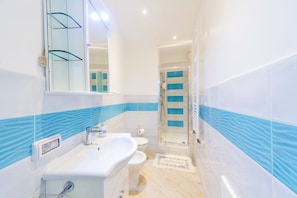 Un baño con lavamanos blanco, espejo, inodoro y cabina de ducha de vidrio.