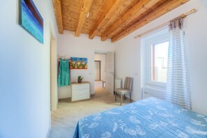 A bedroom with a wooden ceiling, a bed with a blue floral bedspread, a chair, a radiator, and a painting on the wall.