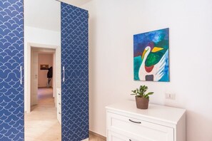 A hallway with a blue patterned door, a white cabinet with a plant, and a colorful abstract painting on the wall.