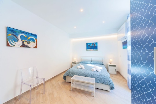 A modern bedroom with a bed, a chair, a bedside table, and artwork on the walls.