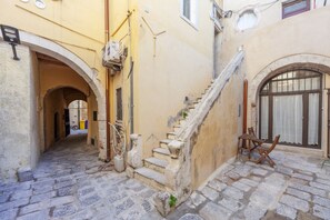 A narrow stone-paved alleyway with a stone staircase leading to a building entrance.