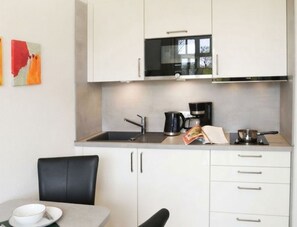 A modern kitchen with white cabinets, a black stove, and a coffee maker. - Apartment Rosenhof 09 - Wh. 09 (Kühlungsborn)