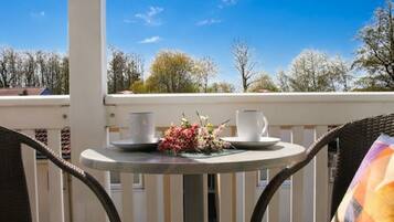 Ein Balkon mit einem Tisch für zwei Personen, bestecktem mit einer weißen Karaffe und Tasse, und einer Blumenkomposition.