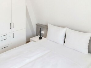 Een minimalistisch ingerichte slaapkamer met een bed, witte beddengoed, een nachtkastje en een kledingkast.