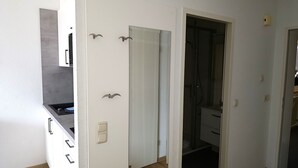 Et moderne køkken med hvide skabe og en sort bordplade, en døråbning til et badeværelse med brusekabine i glas, og trægulv.