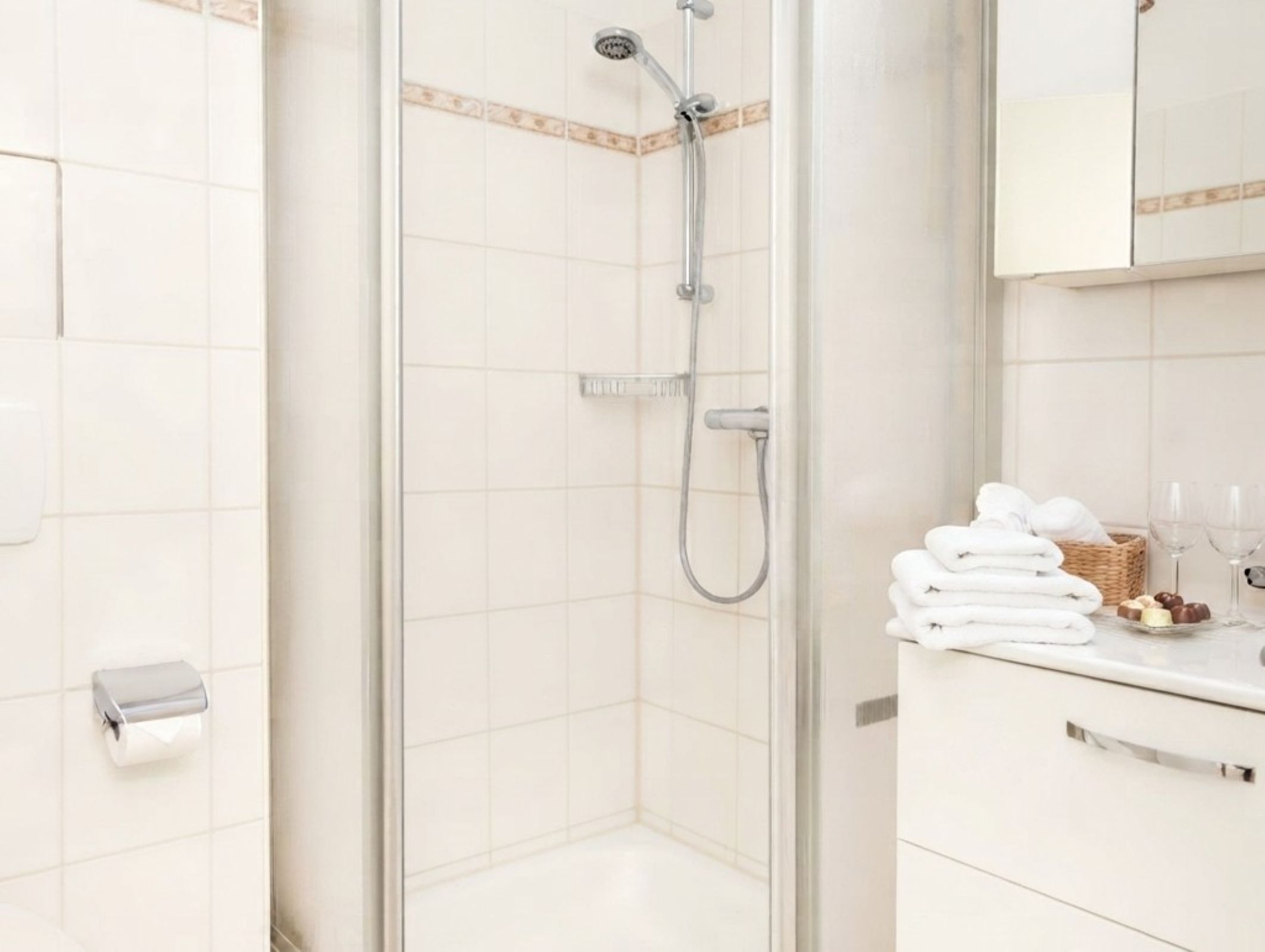 Une salle de bain moderne avec une douche à parois de verre, un porte-rouleau de papier toilette et un meuble avec des serviettes et des articles de toilette.