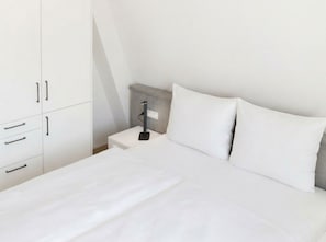 A minimalist bedroom with a bed, white bedding, a nightstand, and a wardrobe. - Rosenhof Apartment 09 - Apt. 09 (Kühlungsborn)