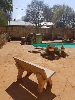 Un área de piscina con un muro de piedra, un banco de madera y plantas en macetas.
