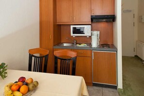 Cocina compacta con armarios de madera, microondas, cafetera y pileta. Hay dos sillas y una mesa con fruta encima.