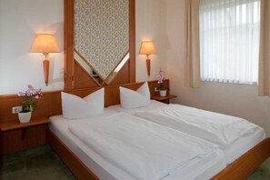 Habitación de hotel con cama doble, dos lámparas de noche, un espejo, una planta en maceta y una ventana con cortinas.