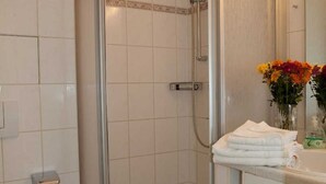 Een badkamer met een douche met glazen wand, een wastafel met spiegel en een vaas met bloemen.