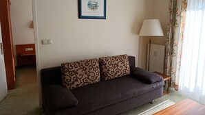 Een woonkamer met een bank, een lamp, een foto aan de muur en een deur die naar een andere kamer leidt.