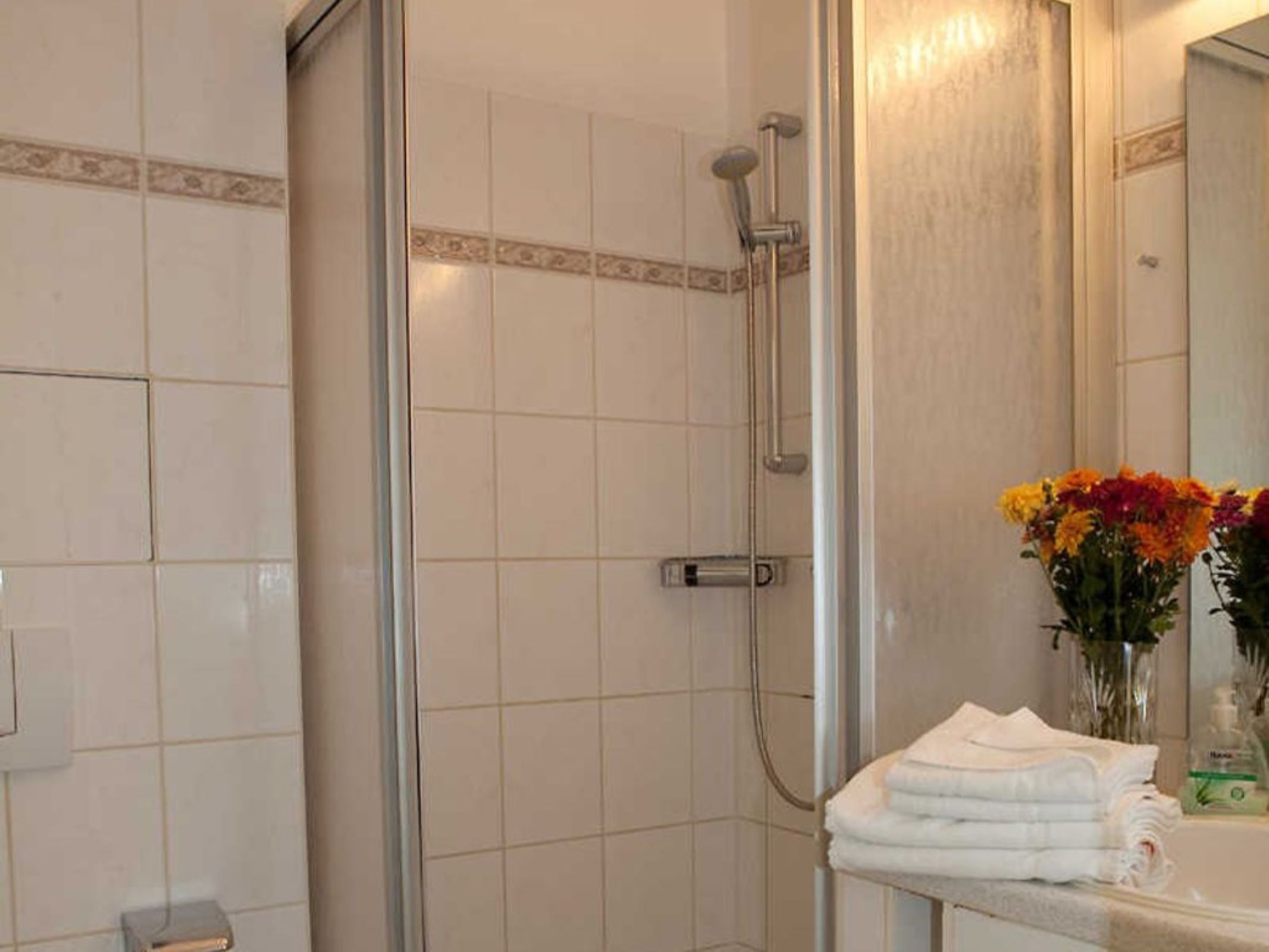 Ein Badezimmer mit Duschkabine, Waschbecken mit Spiegel und Blumen in einer Vase.
