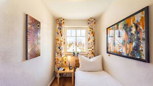A bedroom with a bed, a desk, a window with curtains, and two paintings on the walls. - Apartment Rosenhof 07 - Wh. 07 (Kühlungsborn)