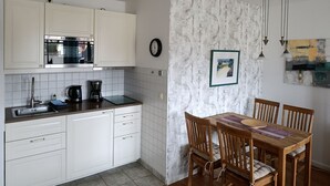 A compact kitchen with white cabinets, a built-in oven, and a dining area with wooden chairs and a table. - Apartment Rosenhof 07 - Wh. 07 (Kühlungsborn)