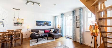 Una sala de estar moderna con un sofá, una mesa de comedor y sillas, una escalera y un ventanal con cortinas.