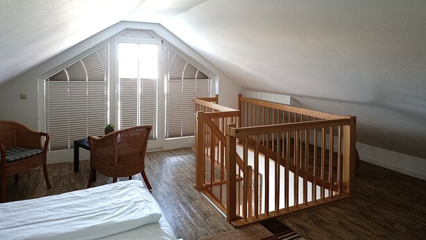 A room with a sloped ceiling, a wooden crib, a bed, two wicker chairs, and a small table with a plant. - Apartment Rosenhof 07 - Wh. 07 (Kühlungsborn)