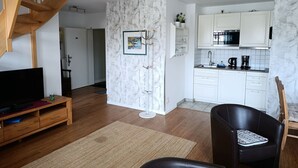 A modern living room with a wooden staircase, a flat-screen TV, a wooden coffee table, and a black leather chair. - Apartment Rosenhof 07 - Wh. 07 (Kühlungsborn)