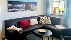 A living room with a black leather sofa, a round coffee table, and a painting of a pier over water. - Apartment Rosenhof 07 - Wh. 07 (Kühlungsborn)