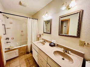 Baño con dos lavamanos, ducha y bañera. Hay dos espejos y un perchero para toallas.