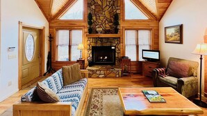 Una sala acogedora con chimenea de piedra, techo de madera y un amplio ventanal.