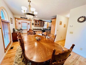 Comedor con mesa y sillas de madera, una lámpara de araña y una cocina al fondo.