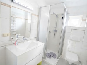 Une salle de bain moderne avec une douche à parois de verre, un lavabo blanc avec un miroir au-dessus et des toilettes.
