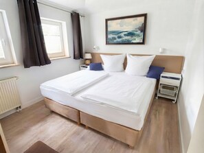 Une chambre d’hôtel avec un grand lit, un tableau au-dessus et une fenêtre avec des rideaux.