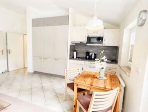 A compact kitchen with a dining table and chairs, a hanging light fixture, and a clock on the wall.