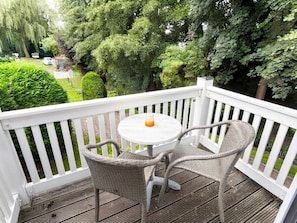 Une terrasse en bois avec une balustrade blanche, une table ronde et deux chaises en osier.