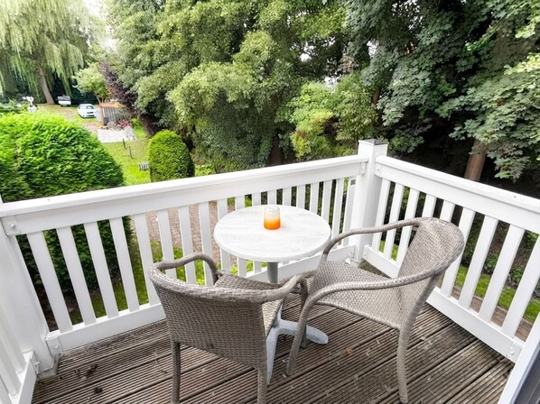A wooden deck with a white railing, a round table, and two wicker chairs.