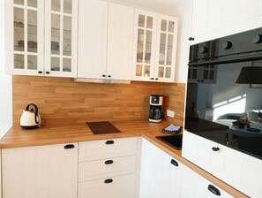 Una cocina con encimeras de madera, armarios blancos, hervidor, cafetera y estufa.