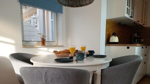 A breakfast setup with a table, chairs, and a window with blinds. - Apartment Rosenhof 12 - Wh. 12 (Kühlungsborn)