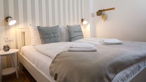 A neatly made bed with pillows, a bedside table with a lamp, and a wall-mounted light fixture. - Apartment Rosenhof 12 - Wh. 12 (Kühlungsborn)