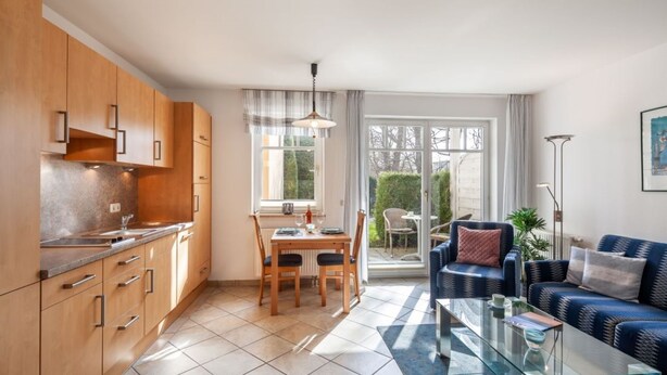 A modern kitchen with wooden cabinets and a dining area with a table and chairs. There is a sofa and a coffee table in the living area. - Apartment Rosenhof 11 - Wh. 11 (Kühlungsborn)