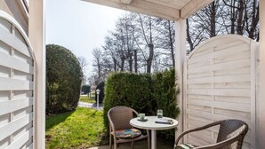 A covered patio with two wicker chairs and a small table, surrounded by a white fence and a hedge. - Apartment Rosenhof 11 - Wh. 11 (Kühlungsborn)