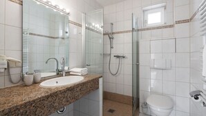 A bathroom with a granite countertop sink, a glass shower enclosure, a toilet, and a mirror with lights. - Apartment Rosenhof 11 - Wh. 11 (Kühlungsborn)