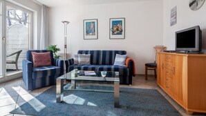A living room with a sofa, armchair, glass coffee table, TV, and wooden cabinet. - Apartment Rosenhof 11 - Wh. 11 (Kühlungsborn)