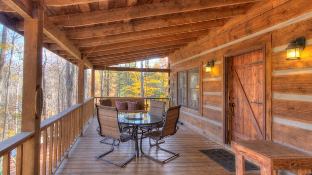 A wooden deck with a table and chairs, a bench, and a view of autumn trees.