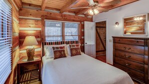 A wooden cabin bedroom with a bed, nightstand, dresser, and a ceiling fan.
