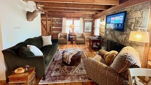A cozy cabin interior with a green sofa, patterned armchair, and a fireplace.