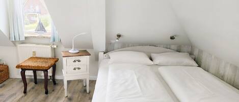A bedroom with a bed, bedside table, chair, and a window with a view of a house.