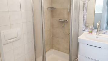 Une douche avec une porte en verre, un lavabo blanc avec un miroir et une serviette sur le sol.