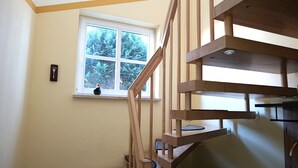Eine Holztreppe mit Blick auf ein Fenster, durch das Bäume zu sehen sind.