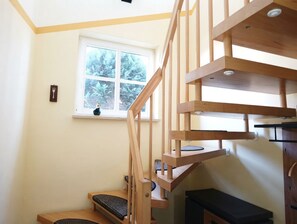 A wooden staircase leading to a loft area with a window overlooking a forest.