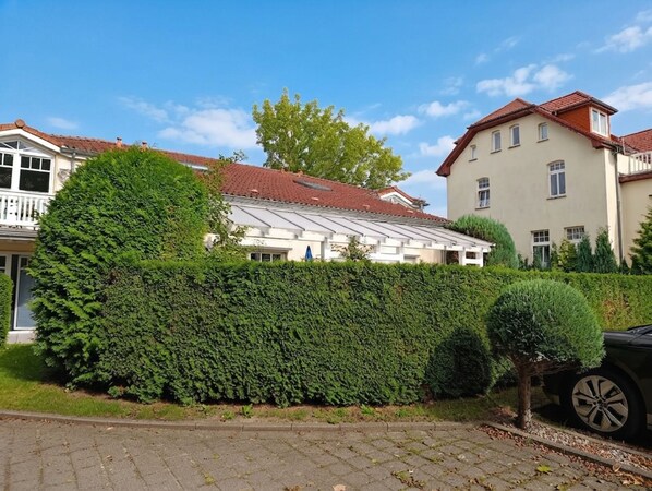 A residential area with a well-maintained hedge, a parked car, and houses with distinct architectural styles.