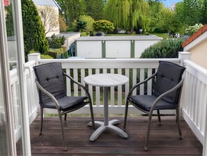 A balcony with two chairs and a small round table, surrounded by a white railing.