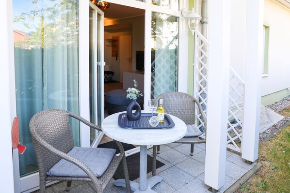 Un espace extérieur aménagé avec des chaises et une table en osier, une bouteille de vin Castiza et un verre.