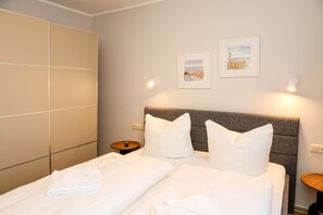 Une chambre d’hôtel comprenant un lit, deux oreillers, une tête de lit, deux tables de chevet et deux appliques murales.